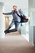 Businessman jumping for joy in office corridor