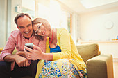 Smiling mature couple texting in living room