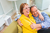 Mature couple laughing and hugging on sofa