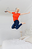 Playful woman jumping on bed listening to music