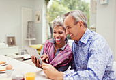 Mature couple sharing digital tablet at breakfast