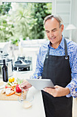 Mature man in apron using digital tablet cooking