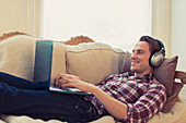 Man with headphones using laptop on sofa