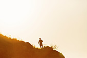 Silhouette of a man running on hill at sunset