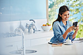 Woman texting with cell phone at kitchen counter