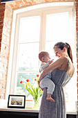 Mother holding baby daughter at window