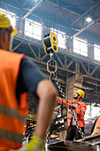 Steel workers operating crane in factory