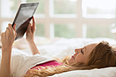 Woman laying in bed using digital tablet