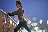 Female runner stretching legs on footbridge