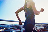 Female runner running on sunny urban footbridge