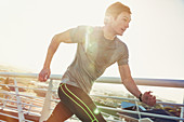 Determined male runner running on sunny footbridge