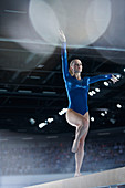 Female gymnast performing on balance beam in arena
