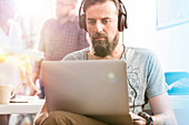Serious male designer with headphones using laptop