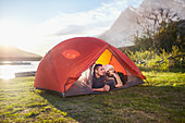 Young couple relaxing in tent at lakeside campsite