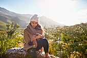 Young woman texting with cell phone on rock