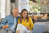 Couple relaxing, using laptop on living room sofa