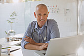 Smiling male doctor working at laptop