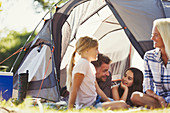 Smiling family talking and relaxing outside tent