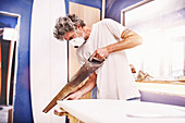 Male surfboard designer and using saw