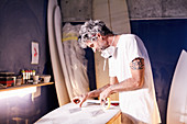 Surfboard designer taping surfboard in workshop