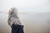 Senior woman with hand in long grey hair on beach