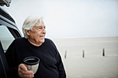 Happy senior man drinking coffee at car on beach