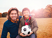 Portrait father and son with soccer ball grass
