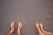 Barefoot couple standing in wet sand on beach