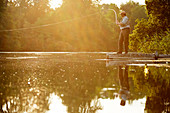Senior man fly fishing on dock of summer lake