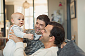 Male gay parents holding baby son on sofa