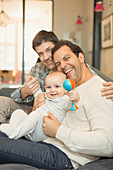 Portrait male gay parents and baby son with rattle