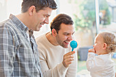 Male gay parents and baby son playing with rattle