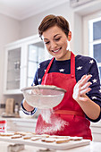 Smiling woman baking, sifting sugar over cookies