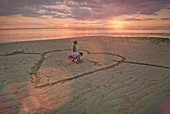 Bbrother and sister drawing heart-shape in sand