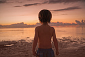 Boy on beach looking at tranquil sunset ocean