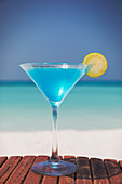 Blue cocktail with lemon slice on beach