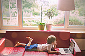 Boy using laptop on red leather sofa