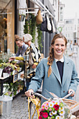 Woman walking bicycle with flowers in basket