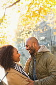 Smiling young couple hugging under autumn tree