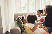 Daughters cuddling mother laying on sofa