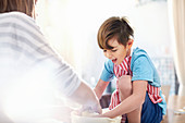 Boy helping mother baking, mixing dough in bowl