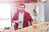 Male carpenter drinking tea, making wood boat