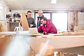 Male carpenters using laptop near wood boat