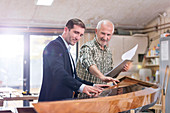 Male carpenter and customer examining wood kayak