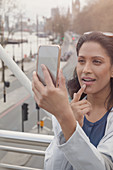Woman checking makeup with camera phone, London