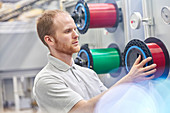 Male worker changing spool in fiber optics factory