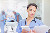 Surgeon with tablet reviewing clipboard paperwork
