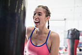 Laughing young female boxer at punching bag in gym