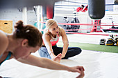 Young women stretching legs next to boxing ring