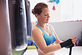 Female boxer wrapping wrists next to punching bag